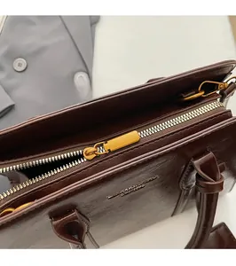Detail of smooth gold zipper and embossed logo on minimalist dark brown leather handbag
