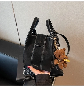 Black leather bucket bag with white contrast stitching and brown plush bear charm