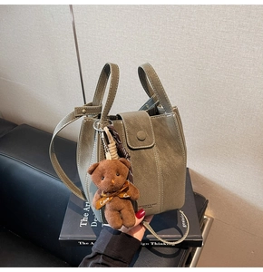 Detailed macro view of olive green bucket bag with plush bear charm and white stitching