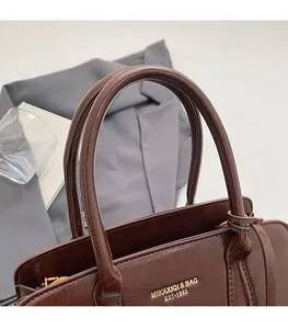 Detail of round handles and gold branding on a brown leather minimalist tote bag