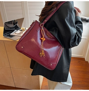 Detail of burgundy glossy tote bag with beaded tassel and metal logo on a model