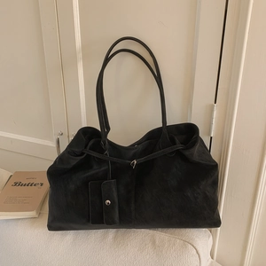 Detail of minimalist black matte tote bag with matching coin purse on soft white fabric