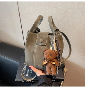 Detail view of mini dark green bucket bag with plush bear charm and woven rope accessory