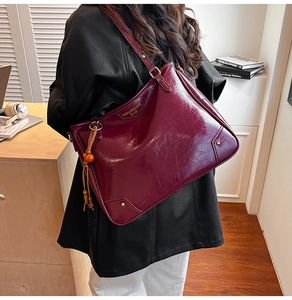 Close-up of burgundy tote bag showing glossy oil wax leather texture and tassel detail