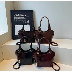 Close-up of leather bucket bags featuring knotted handles and plush pompom charms