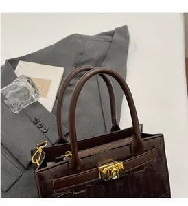 Detail of dark brown crocodile embossed handbag with metal lock and double top handles