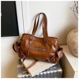 Detail of vintage cognac tote bag with side buckle pockets and textured leather on a suitcase
