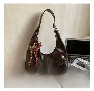 Detail of dark brown glossy underarm bag with silver rivets and bear charm accessory