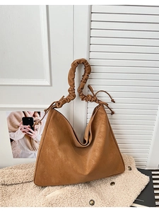 Brown suede tote bag with ruched handle and side tie detail on fuzzy jacket background