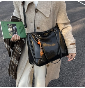 Detailed close-up of glossy black tote bag with orange beaded tassel and gold hardware