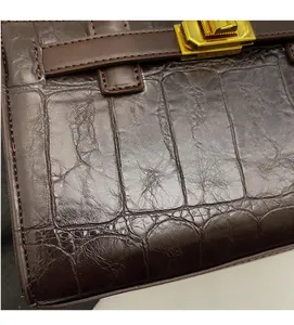 Detail of dark brown crocodile embossed leather bag with gold twist lock and stitching