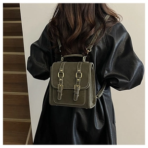 Dark green vintage leather backpack with buckle detail worn by model on a modern staircase