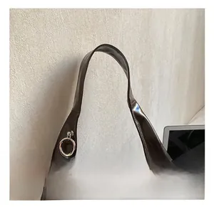 Detail of wide handles and animal charm on a large dark brown polished leather tote bag