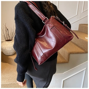 Detail showing high-capacity burgundy shoulder bag in glossy faux leather on a model