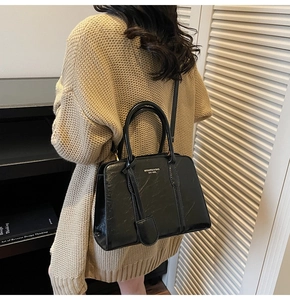Polished black tote bag with gold logo shown on model wearing beige knit sweater