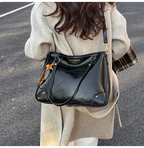 Detail of black patent leather tote bag with gold hardware and wood bead tassel
