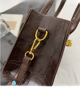 Close-up of deep brown crocodile embossed leather bag with shiny gold metal hook buckle