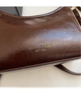 Dettaglio borsa sottobraccio in pelle marrone scuro con logo dorato e texture ricercata
