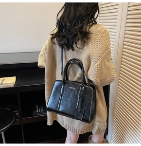 Model wearing a black vintage textured leather tote bag with a golden brand logo