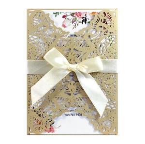 Detailed laser-cut vine patterns on gold wedding invitation with satin ribbon bow