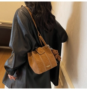 Brown bucket bag with white stitching detail and a plush bear pendant on shoulder strap