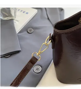 Detail of glossy brown leather bucket bag with luxury golden lobster clasp hardware