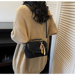 Detail of black matte suede crossbody bag with ethnic beaded charm and letter embossing