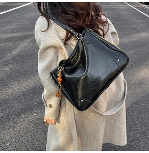 Detail of black glossy leather tote bag with unique wood bead tassel and gold rivet accents
