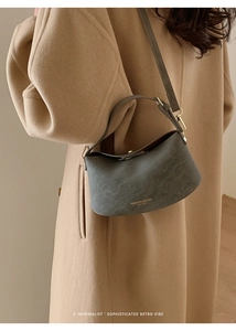 Close-up of minimalist grey crescent shoulder bag with golden text on matte leather