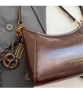 Dettaglio ravvicinato della borsa a mezzaluna in pelle cerata marrone con ciondolo oro