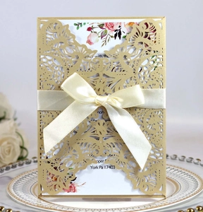 Detail of laser-cut wedding invitation with gold sleeve and white satin ribbon bow