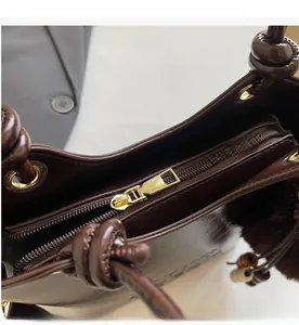 Detail of smooth gold zipper closure and plush charm on brown leather bucket bag
