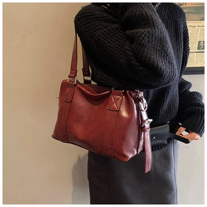 Close-up of wine red leather tote bag with X-stitch reinforced handles worn with sweater