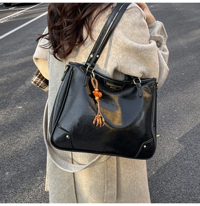 Detail of glossy black tote bag with vintage texture and orange bead tassel accessory