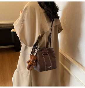 Detail of dark brown matte bucket bag with white stitching and cute bear charm