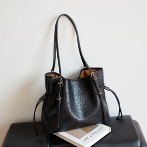 Detail of black ostrich embossed leather tote with gold hardware and side lace accents