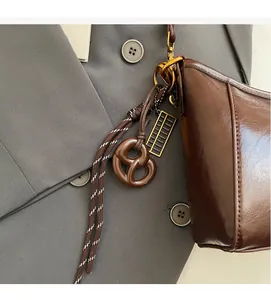 Dettaglio borsa marrone lucida con ciondoli a forma di pretzel e abaco dorato