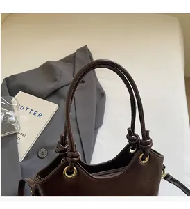 Detail of a dark brown glossy bucket bag featuring a knotted handle and gold eyelets