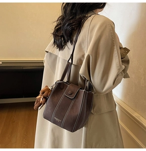 Detail of brown leather bucket bag with contrast stitching and plush bear charm