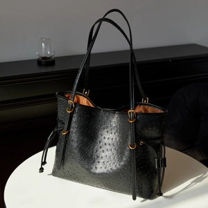 Detail of black ostrich-textured tote bag with gold ring and brown lining on a white table