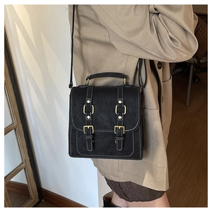 Detail of vintage black messenger backpack with contrast stitching and gold buckles
