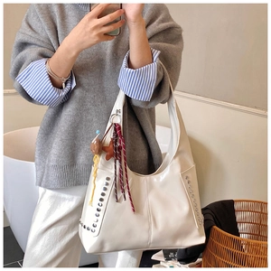Détail du sac hobo blanc avec rivets argentés et breloques dans un décor intérieur doux