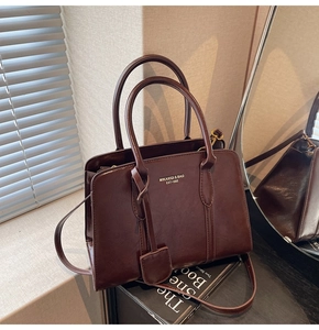 Detail of dark brown leather tote bag showing gold logo and detachable shoulder strap