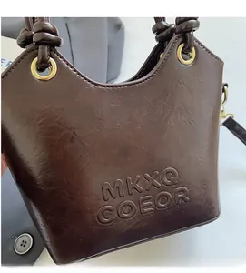 Detail of dark brown glossy bucket bag featuring knot handle and MKXQ COEOR embossed logo