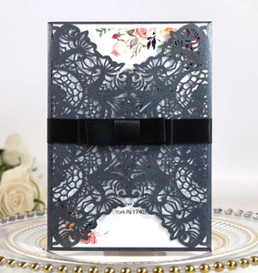 Detail of laser-cut wedding invitation with dark glitter cover and black silk ribbon