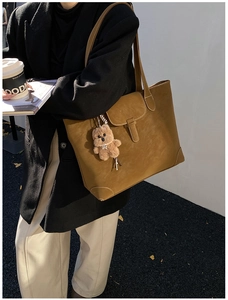 Detail of vintage brown suede tote bag featuring metal buckle and cute bear pendant decoration