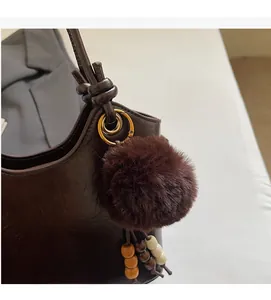 Detail of dark brown leather bucket bag with plush pom-pom charm and embossed lettering