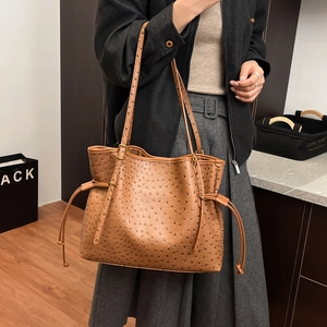 Detail of brown ostrich leather tote bag featuring golden buckle and drawstring design