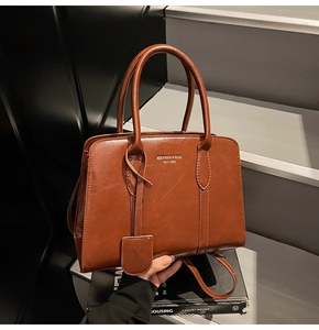 Detailed close-up of a caramel brown faux leather handbag with dual handles and gold lettering
