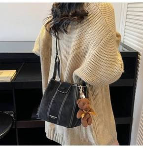 Detail of black bucket bag with contrast stitching and plush bear charm on a model